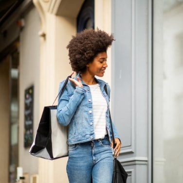 A girl in jeans walking and smiling with shopping bags